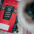 Load image into Gallery viewer, bag of cannonball coffee on a tablecloth with coffee beans scattered around. Next to it is a v60 coffee maker